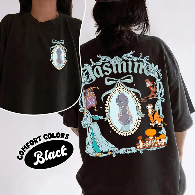 May include: Black Comfort Colors t-shirt featuring a front and back design. The front has a small oval illustration with a bow. The back has a larger design with the word "Jasmine" and illustrations of characters and objects from the movie.