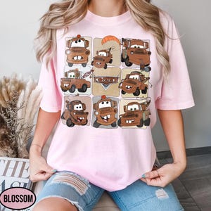 Może przedstawiać: Jasnor&oacute;żowa koszulka z wzorem kratki przedstawiającym kresk&oacute;wkowe obrazy Złomka z filmu Auta. Obrazy są w odcieniach brązu i beżu, ze słowem "Cars" pośrodku.