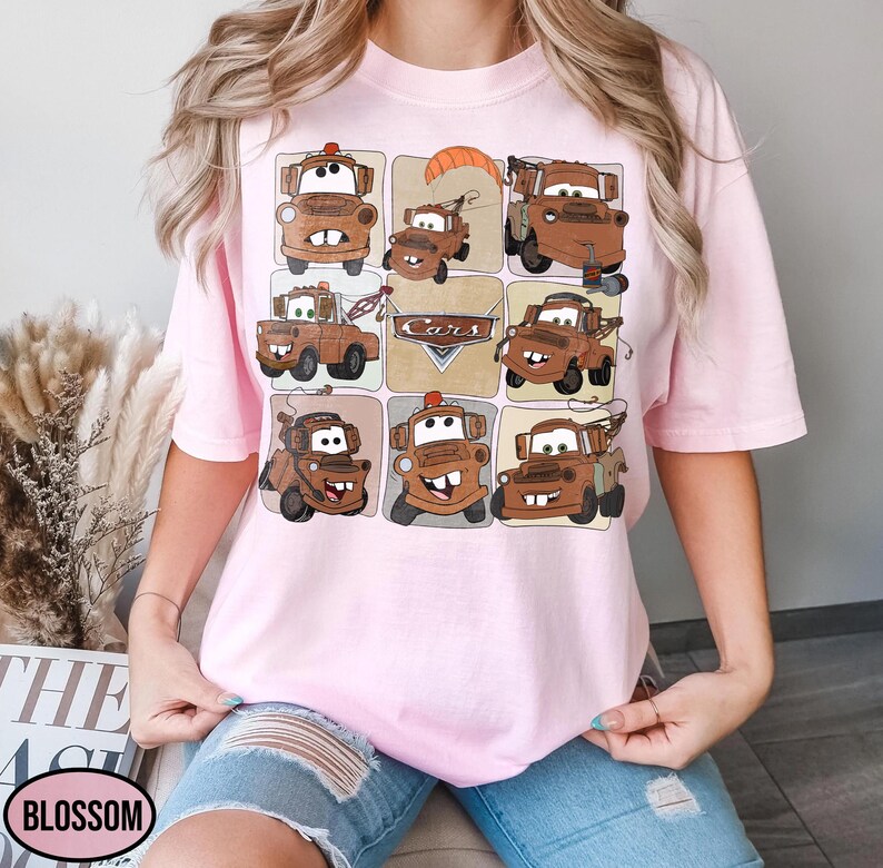 Może przedstawiać: Jasnor&oacute;żowa koszulka z wzorem kratki przedstawiającym kresk&oacute;wkowe obrazy Złomka z filmu Auta. Obrazy są w odcieniach brązu i beżu, ze słowem "Cars" pośrodku.