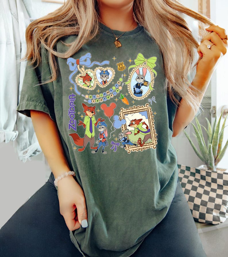 May include: Dark green t-shirt featuring characters from the movie Zootopia. The shirt has a colorful graphic design with framed images of the characters, the word "Zootopia", and Mickey Mouse balloons.