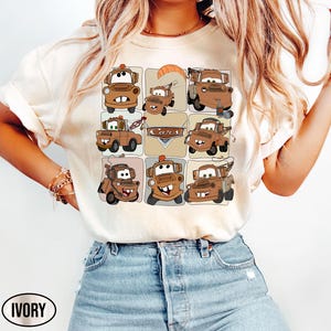 Może przedstawiać: Kremowa koszulka z siatką z kresk&oacute;wkowymi obrazkami postaci Złomka z filmu Auta. Słowo "Cars" jest wydrukowane na beżowym banerze. Koszulka ma kr&oacute;tkie rękawy i okrągły dekolt.