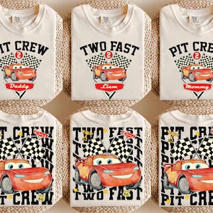 May include: Off-white t-shirts with race car graphics. Some shirts say "Pit Crew" with "Daddy" or "Mommy" below. Others say "Two Fast" with "Liam" below. Checkered flags and the number 2 are also featured.