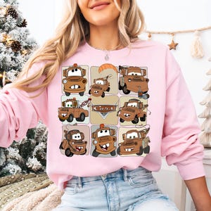 Może przedstawiać: R&oacute;żowa bluza z długim rękawem z siatką ilustracji samochod&oacute;w z kresk&oacute;wek w odcieniach brązu i beżu. Na wzorze nadrukowano napis "Cars". Bluza wykonana jest z miękkiego materiału.