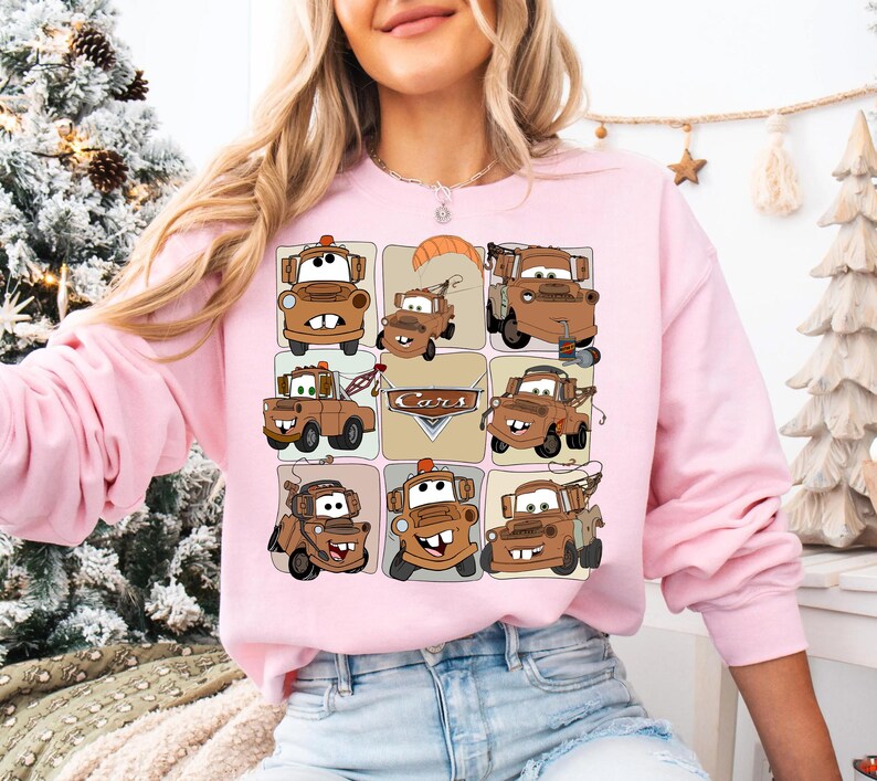 Może przedstawiać: R&oacute;żowa bluza z długim rękawem z siatką ilustracji samochod&oacute;w z kresk&oacute;wek w odcieniach brązu i beżu. Na wzorze nadrukowano napis "Cars". Bluza wykonana jest z miękkiego materiału.