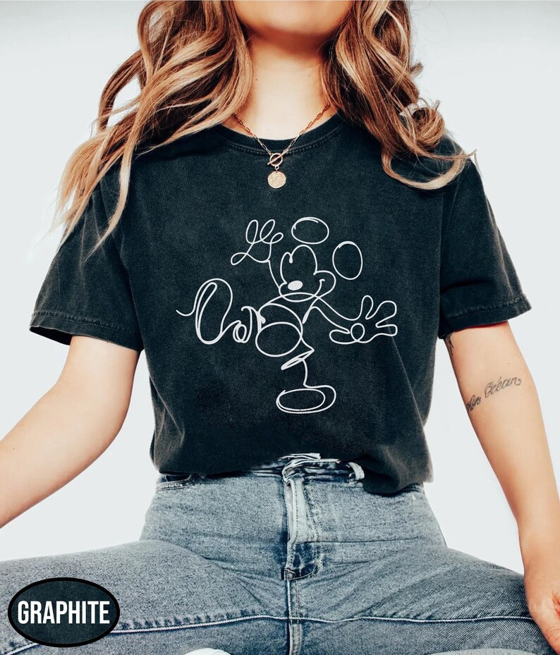 May include: Graphite-colored t-shirt featuring a white line drawing of Mickey Mouse. The design includes the character's outline and the word "Oh" in a cursive font. The shirt is paired with blue denim jeans.