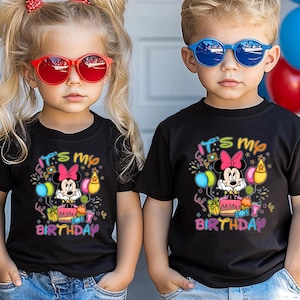 May include: Two children wearing black t-shirts with a Minnie Mouse birthday design. The shirts feature the text "It's my Birthday" with colorful graphics. One child wears red sunglasses, the other blue.