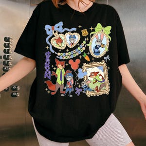 May include: Black t-shirt featuring colorful cartoon illustrations of characters from the movie Zootopia. The design includes framed portraits, a police badge, and the word "Zootopia" in purple. The shirt has a crew neck and short sleeves.