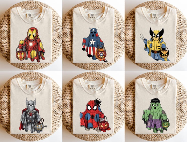 Op de afbeelding: Zes gevouwen cr&egrave;mekleurige T-shirts met superhelden-geestontwerpen. Elk shirt heeft een ander personage: Iron Man, Captain America, Wolverine, Thor, Spider-Man en Hulk, elk met een Halloween pompoenemmer.
