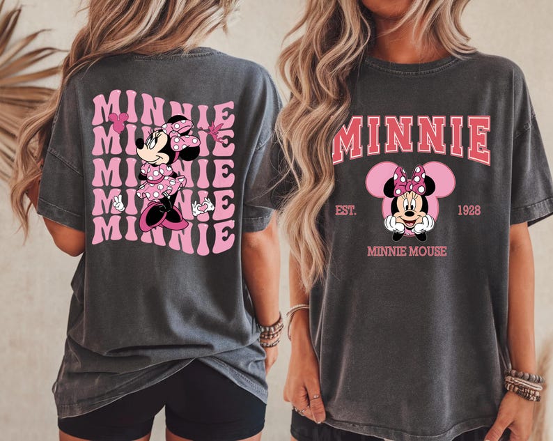May include: Dark gray t-shirts featuring Minnie Mouse. One shirt has a pink and white design with the word "Minnie" repeated. The other shirt has a Minnie Mouse graphic with the word "Minnie" above and "Minnie Mouse" below.