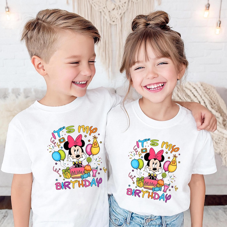 May include: Two children wearing white t-shirts with a colorful Minnie Mouse birthday design. The design includes Minnie Mouse, balloons, a cake, and the text "It's my birthday".