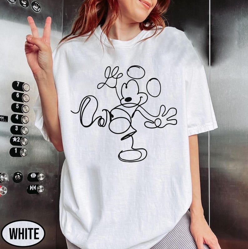May include: White t-shirt featuring a black line drawing of Mickey Mouse. The design shows Mickey with his arms outstretched and the word "Oh" in cursive. The shirt is a casual style, with short sleeves.