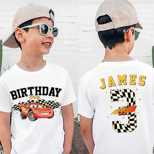 May include: White t-shirt featuring a red cartoon race car with the text "BIRTHDAY Boy". The back of the shirt displays the name "JAMES", the number "3", and a checkered flag design. The number "95" is also included.