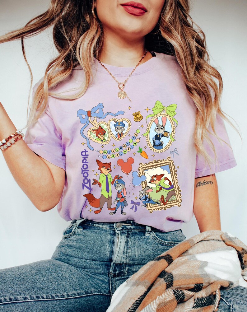 May include: A light purple t-shirt featuring characters from the animated movie Zootopia. The design includes framed images of the characters, along with the word "Zootopia" in a vertical font. The shirt is made of a soft material.