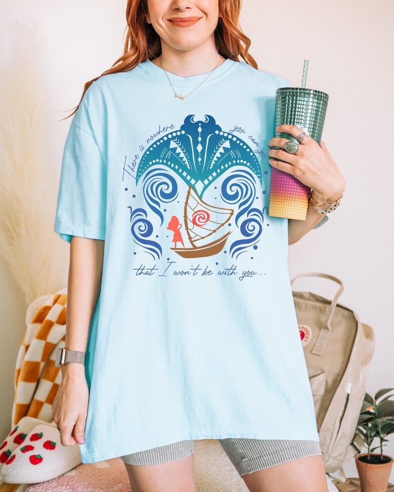May include: Light blue t-shirt with a graphic design featuring a boat, waves, and the text "There is nowhere you can that I won't be with you...". The design is in shades of blue, brown, and red.
