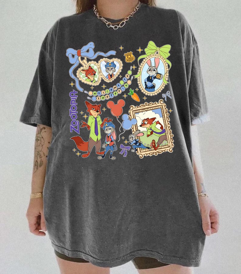 May include: Dark gray Zootopia graphic t-shirt featuring cartoon characters Nick Wilde and Judy Hopps. The design includes framed portraits, balloons, and the word "Zootopia" in a stylized font. The shirt has short sleeves and a relaxed fit.