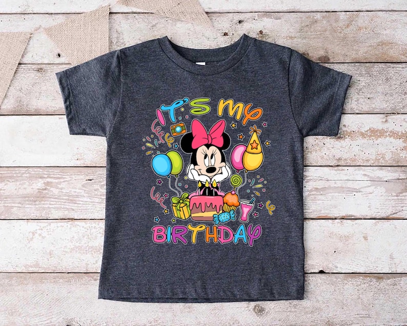 May include: Dark gray t-shirt featuring a colorful graphic of Minnie Mouse with a pink bow, a birthday cake, and balloons. The text "It's my birthday" is written in a playful font. A fun, festive design for a child's birthday.