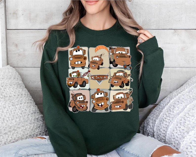 Może przedstawiać: Ciemnozielona bluza z siatką z kresk&oacute;wkowymi obrazami Złomka z filmu Auta. Obrazy są w odcieniach brązu i beżu, ze słowem "Cars" w beżowym prostokącie.