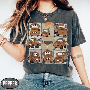 Może przedstawiać: Ciemnoszara koszulka z siatką brązowych kresk&oacute;wkowych w&oacute;zk&oacute;w holowniczych i napisem "Cars". Koszulka ma wygląd vintage, jest wyblakła i wykonana z miękkiego materiału.