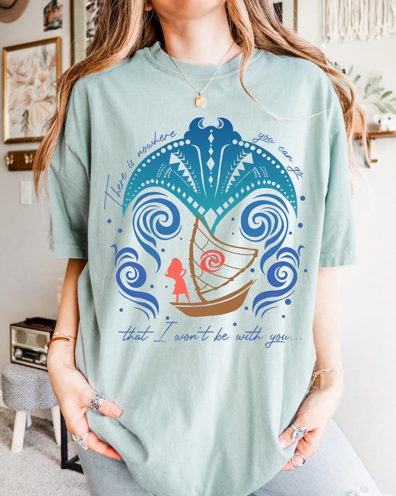 May include: A light green t-shirt featuring a boat with a character illustration and the text "There is nowhere you can go that I won't be with you...". The design includes blue waves and decorative elements.