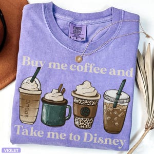 Puede incluir: Una camiseta violeta Comfort Colors con el texto "Buy me coffee and Take me to Disney". La camiseta presenta ilustraciones de cuatro bebidas de caf&eacute; diferentes. Un collar de oro est&aacute; drapeado sobre la camiseta.