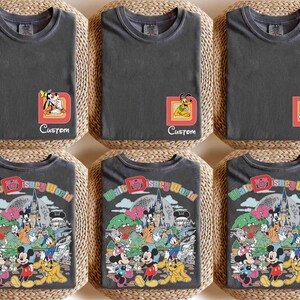 May include: Six charcoal gray t-shirts. The top row features character designs with custom names. The bottom row displays a colorful graphic of Disney characters and the text "Walt Disney World". Each shirt is folded on a woven mat.