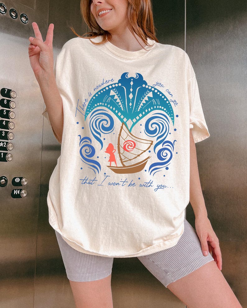 May include: Cream-colored t-shirt featuring a blue and teal graphic of a boat with a character, surrounded by waves and a palm tree design. The text "There is nowhere you can go that I won't be with you..." is printed on the shirt.