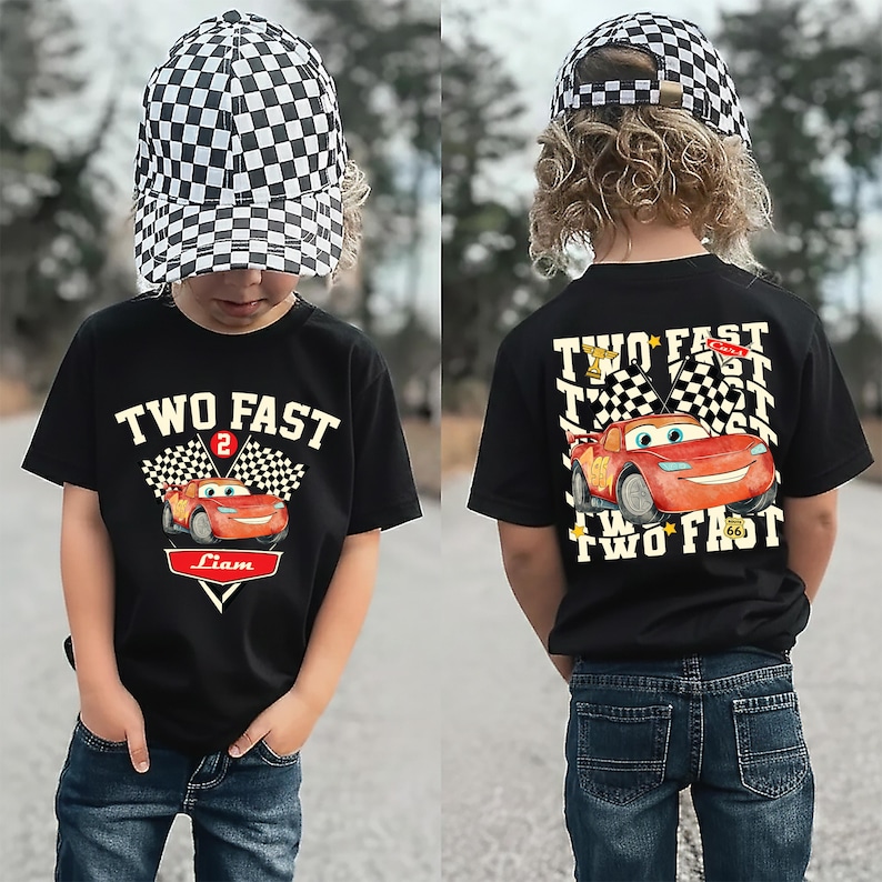 May include: Black t-shirt featuring a red race car graphic and the text "TWO FAST" and "Liam". The outfit includes a black and white chequered baseball cap. The back of the shirt also has the race car and the words "TWO FAST".