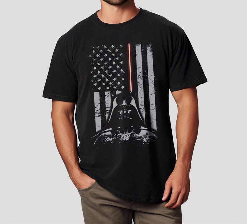 May include: Black t-shirt featuring a distressed American flag design with Darth Vader's helmet and a red lightsaber. The graphic is in shades of gray and white, creating a vintage look. The shirt is made of a soft material.