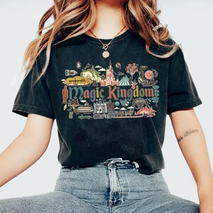 May include: Black t-shirt featuring a colorful graphic of the Magic Kingdom. The design includes various park icons and the words "Magic Kingdom" in a vintage style. The shirt is made of a soft material and has a classic crew neck.
