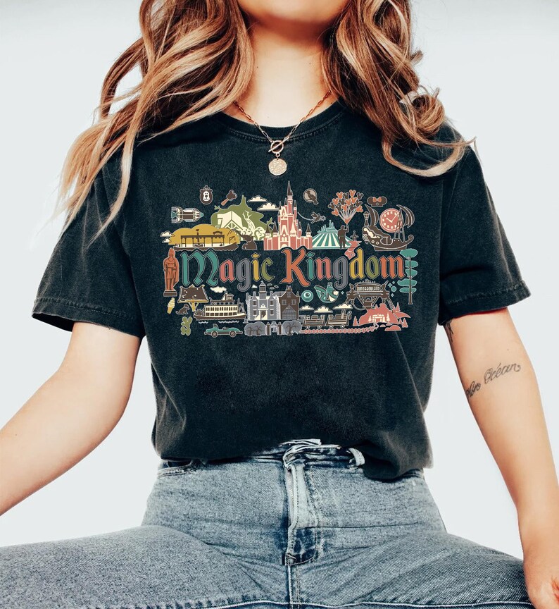 May include: Black t-shirt featuring a colorful graphic of the Magic Kingdom. The design includes various park icons and the words "Magic Kingdom" in a vintage style. The shirt is made of a soft material and has a classic crew neck.