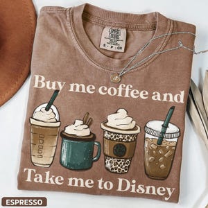 Puede incluir: Camiseta marr&oacute;n con el texto "Buy me coffee and Take me to Disney". La camiseta presenta ilustraciones de cuatro bebidas de caf&eacute; diferentes. Un collar plateado est&aacute; drapeado sobre la camiseta. La palabra "ESPRESSO" est&aacute; en la parte inferior.