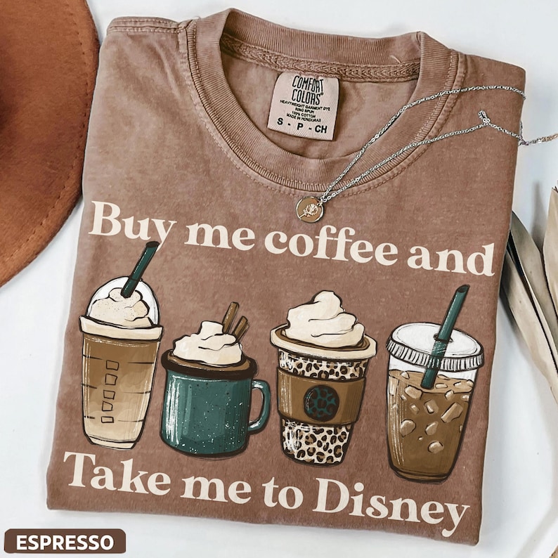 Puede incluir: Camiseta marr&oacute;n con el texto "Buy me coffee and Take me to Disney". La camiseta presenta ilustraciones de cuatro bebidas de caf&eacute; diferentes. Un collar plateado est&aacute; drapeado sobre la camiseta. La palabra "ESPRESSO" est&aacute; en la parte inferior.