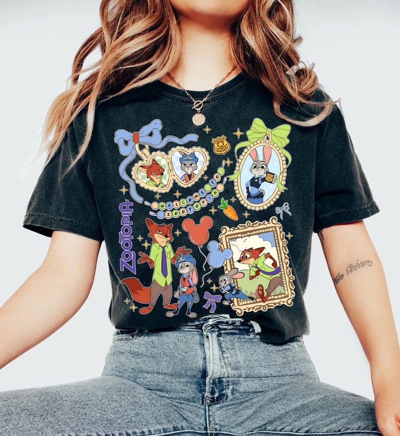 May include: Black t-shirt featuring colorful illustrations of characters from the animated film Zootopia. The design includes framed portraits, a carrot, and the word "Zootopia" in a decorative font. The shirt has a vintage, worn look.