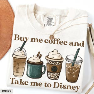 Puede incluir: Camiseta de color marfil con el texto "Buy me coffee and Take me to Disney". La camiseta presenta ilustraciones de cuatro bebidas de caf&eacute; diferentes. Un collar dorado est&aacute; drapeado sobre la camiseta.