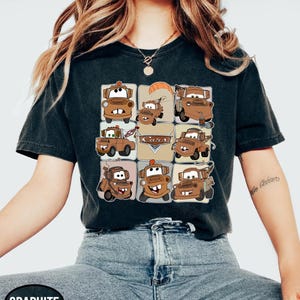 Może przedstawiać: Ciemnoszara koszulka z siatką brązowych kresk&oacute;wkowych lawet z napisem "Cars" pośrodku. Koszulka wykonana jest z miękkiego materiału i nadaje się do noszenia na co dzień.