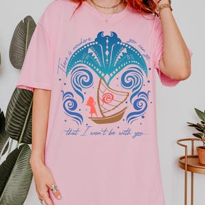 May include: Pink t-shirt featuring a graphic design with a boat, waves, and palm tree elements. The design includes the text "There is nowhere you can go that I won't be with you..."
