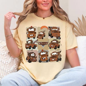 Może przedstawiać: Jasnoż&oacute;łta koszulka z siatką dziewięciu kresk&oacute;wkowych obraz&oacute;w postaci Złomka z filmu Auta. Obrazy są w odcieniach brązu i beżu, ze słowem "Cars" pośrodku.