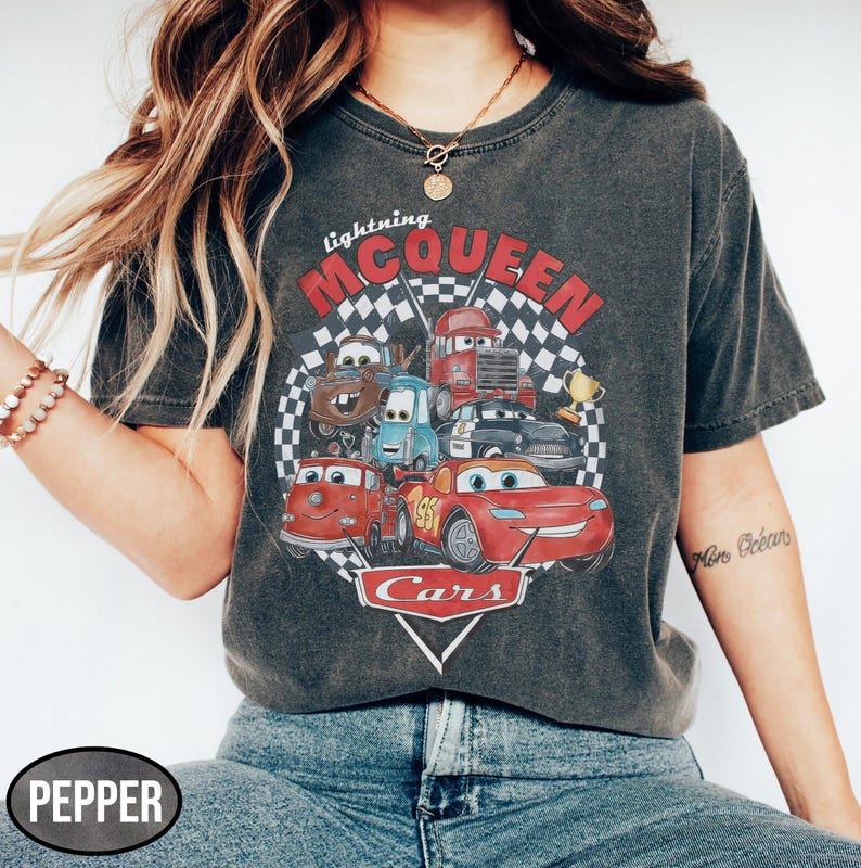 Puede incluir: Camiseta gris oscuro con un gr&aacute;fico de personajes de la pel&iacute;cula Cars, incluyendo a Rayo McQueen. El dise&ntilde;o incluye el texto "Lightning McQueen" y "Cars" en un tema de carreras. La camiseta tiene un aspecto vintage y desgastado.