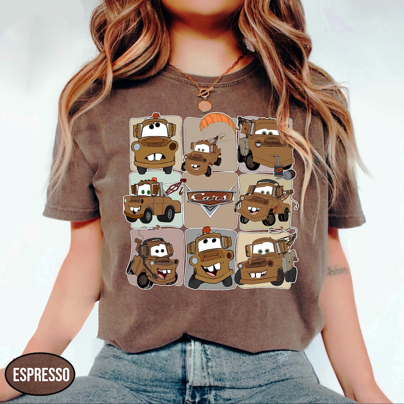 Może przedstawiać: Koszulka w kolorze espresso z siatką kresk&oacute;wkowych woz&oacute;w holowniczych w r&oacute;żnych pozach. Słowo "Cars" jest wyświetlane w brązowo-beżowej odznace. Koszulka ma kr&oacute;tkie rękawy i okrągły dekolt.