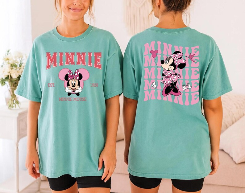 May include: A teal t-shirt featuring Minnie Mouse. The front of the shirt has the word "MINNIE" in pink block letters above a graphic of Minnie Mouse. The back of the shirt has a repeating pink graphic of Minnie Mouse with the word "MINNIE".