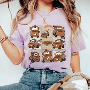 Może przedstawiać: Jasnofioletowa koszulka z siatką z kresk&oacute;wkowymi obrazami postaci Złomka z filmu Auta. Słowo "Cars" jest r&oacute;wnież widoczne na koszulce. Koszulka jest wykonana z miękkiego materiału.