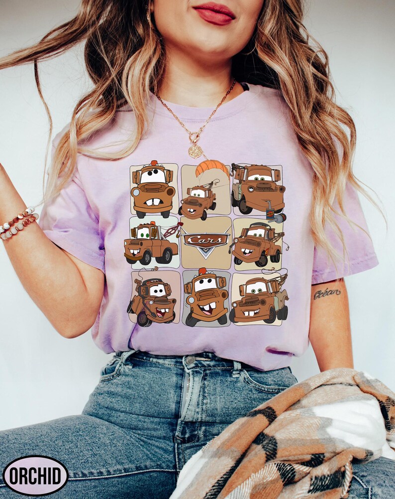 Może przedstawiać: Jasnofioletowa koszulka z siatką z kresk&oacute;wkowymi obrazami postaci Złomka z filmu Auta. Słowo "Cars" jest r&oacute;wnież widoczne na koszulce. Koszulka jest wykonana z miękkiego materiału.