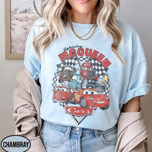 Puede incluir: Camiseta azul claro con un gr&aacute;fico de Rayo McQueen y otros personajes de la pel&iacute;cula Cars. El dise&ntilde;o incluye el texto "lightning McQueen" y "Cars" con un fondo de bandera a cuadros. La camiseta es de color azul claro.