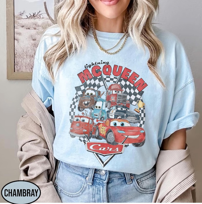 Puede incluir: Camiseta azul claro con un gr&aacute;fico de Rayo McQueen y otros personajes de la pel&iacute;cula Cars. El dise&ntilde;o incluye el texto "lightning McQueen" y "Cars" con un fondo de bandera a cuadros. La camiseta es de color azul claro.