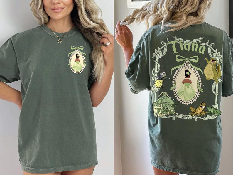 May include: Olive green t-shirt featuring a front and back design. The front has a cameo of a princess in a green dress. The back displays the word "Tiana" and other characters from the movie "Princess and the Frog".