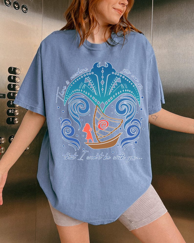 May include: A light blue t-shirt featuring a colorful graphic design with the text "There is nowhere you can go that I won't be with you...". The design includes a boat, waves, and a stylized sun.