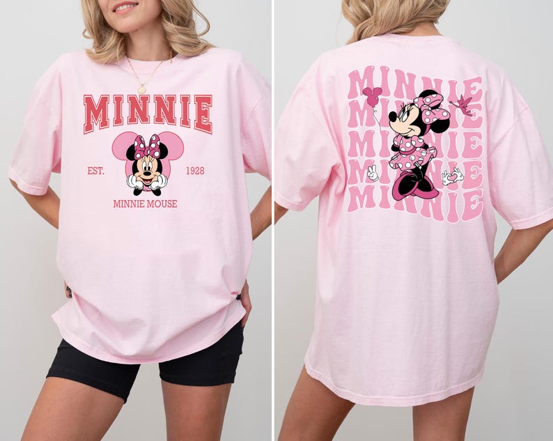 May include: A light pink t-shirt featuring Minnie Mouse. The front of the shirt has the word "MINNIE" in red block letters above a Minnie Mouse graphic. The back of the shirt has a larger Minnie Mouse graphic and the word "MINNIE" repeated.