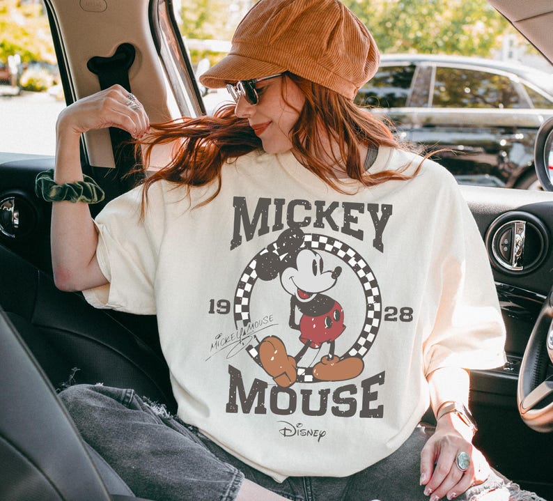 May include: Cream-colored Mickey Mouse t-shirt with a distressed graphic. The design features Mickey Mouse in a circle with a checkered border, the words "Mickey Mouse," and the Disney logo. The shirt has short sleeves.