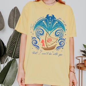 May include: Yellow t-shirt with a graphic design featuring a boat, a figure, and ocean waves. The text on the shirt reads "There is nowhere you can go that I won't be with you..."