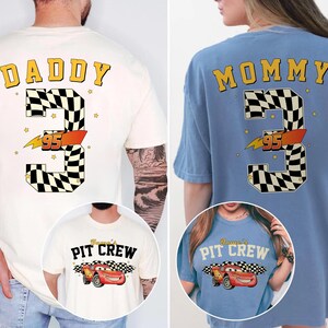 May include: Two t-shirts, one cream and one blue, featuring a racing theme. The cream shirt says "DADDY" above a large number "3" with a checkered pattern and "95" in orange. The blue shirt says "MOMMY" with the same design.